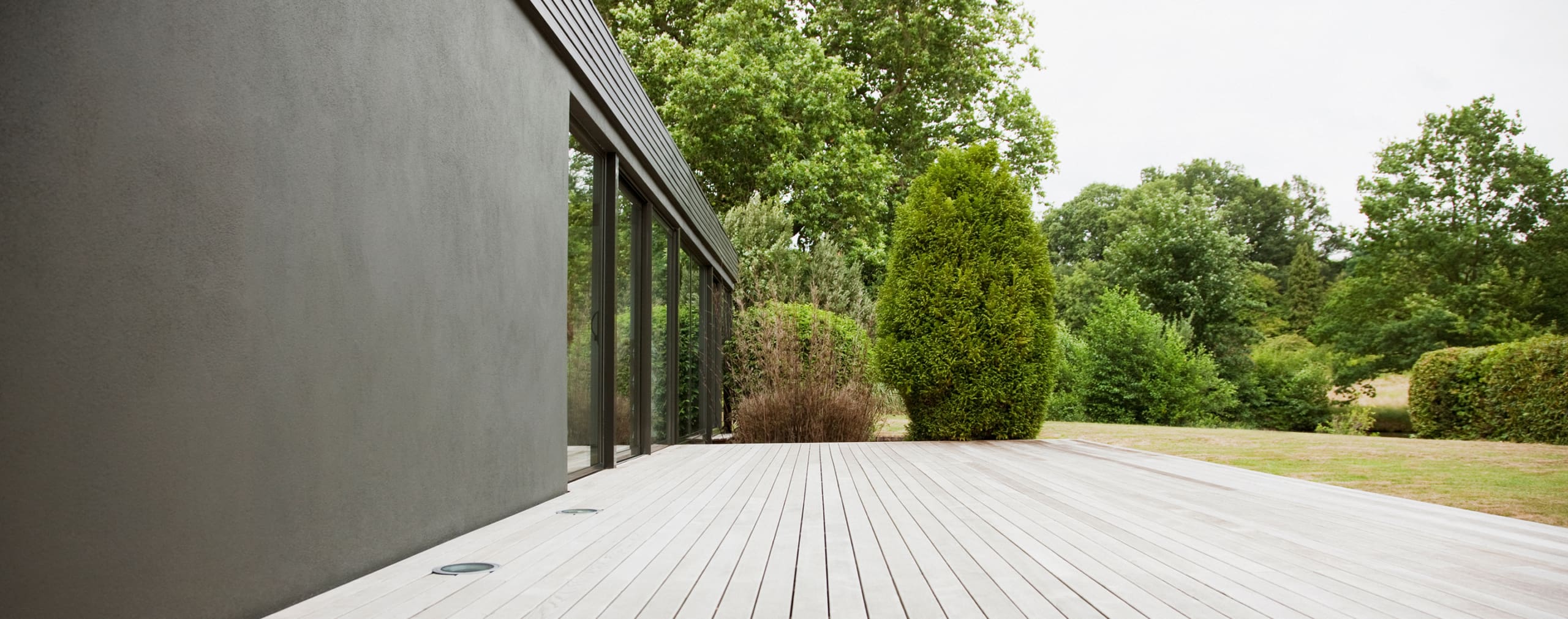 Modern dark exterior home with large windows and a wooden deck